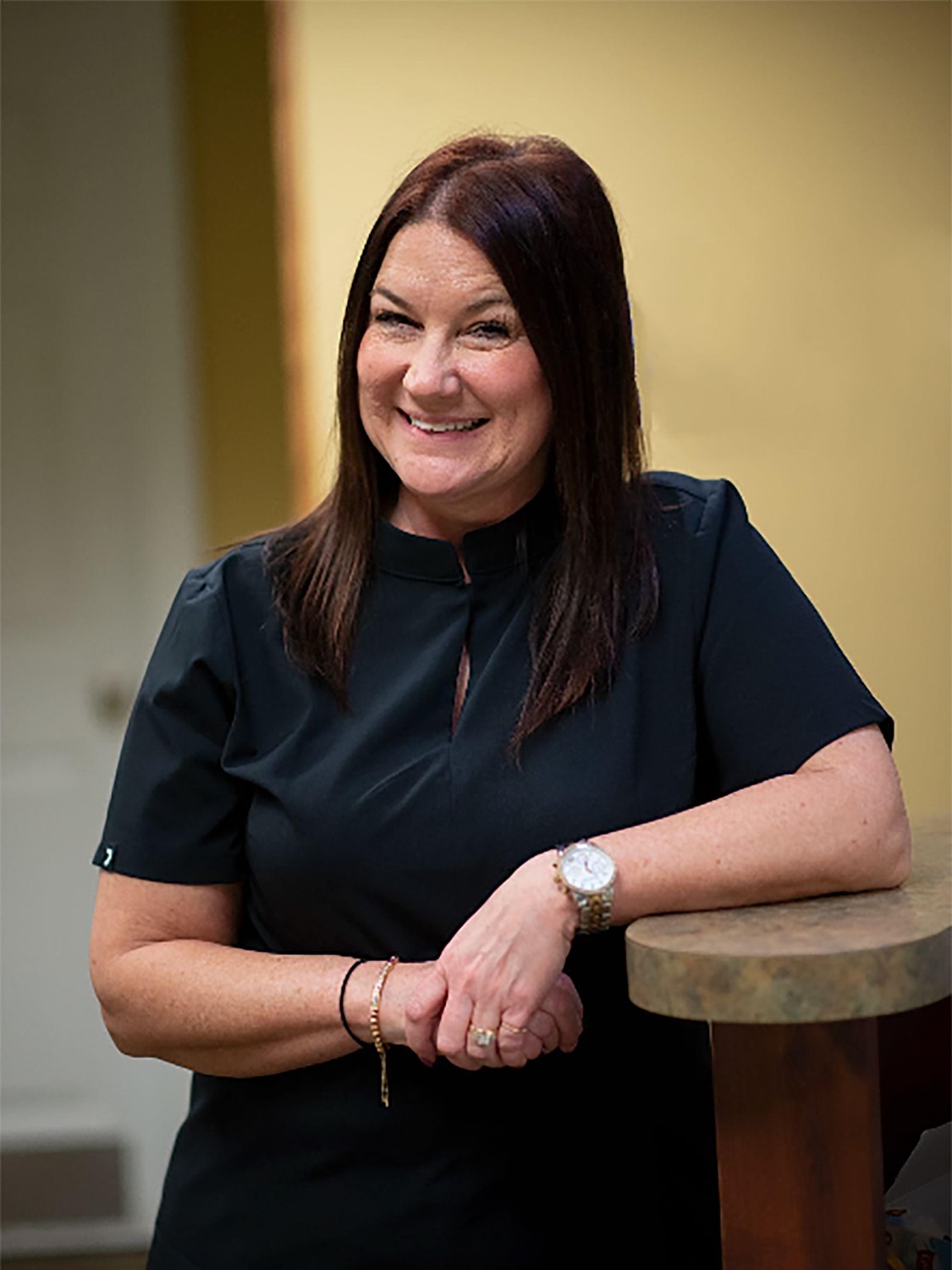 Smiling woman in a professional outfit leaning on counter.