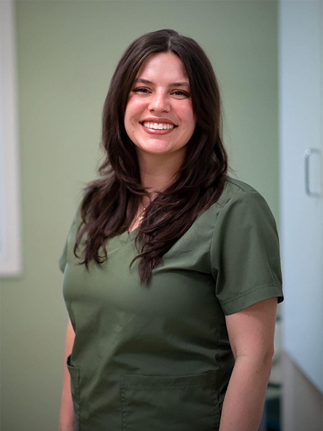 Smiling woman in green scrubs standing indoors.
