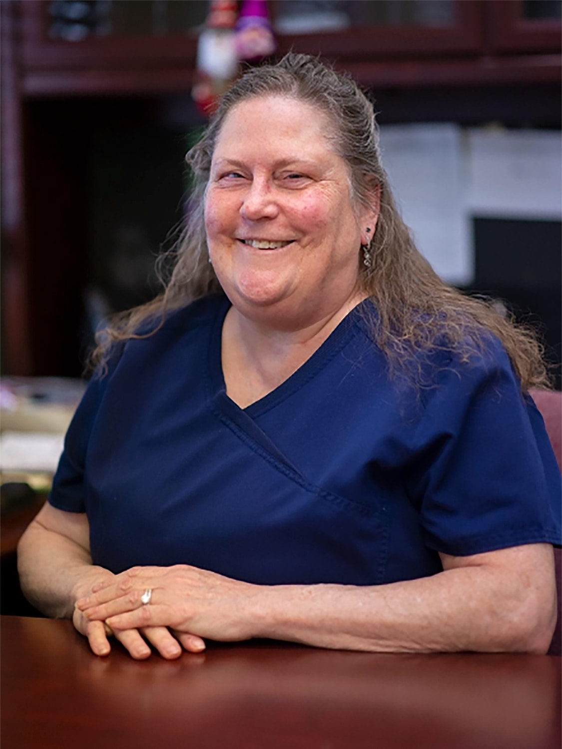 Smiling woman in medical scrubs at desk.